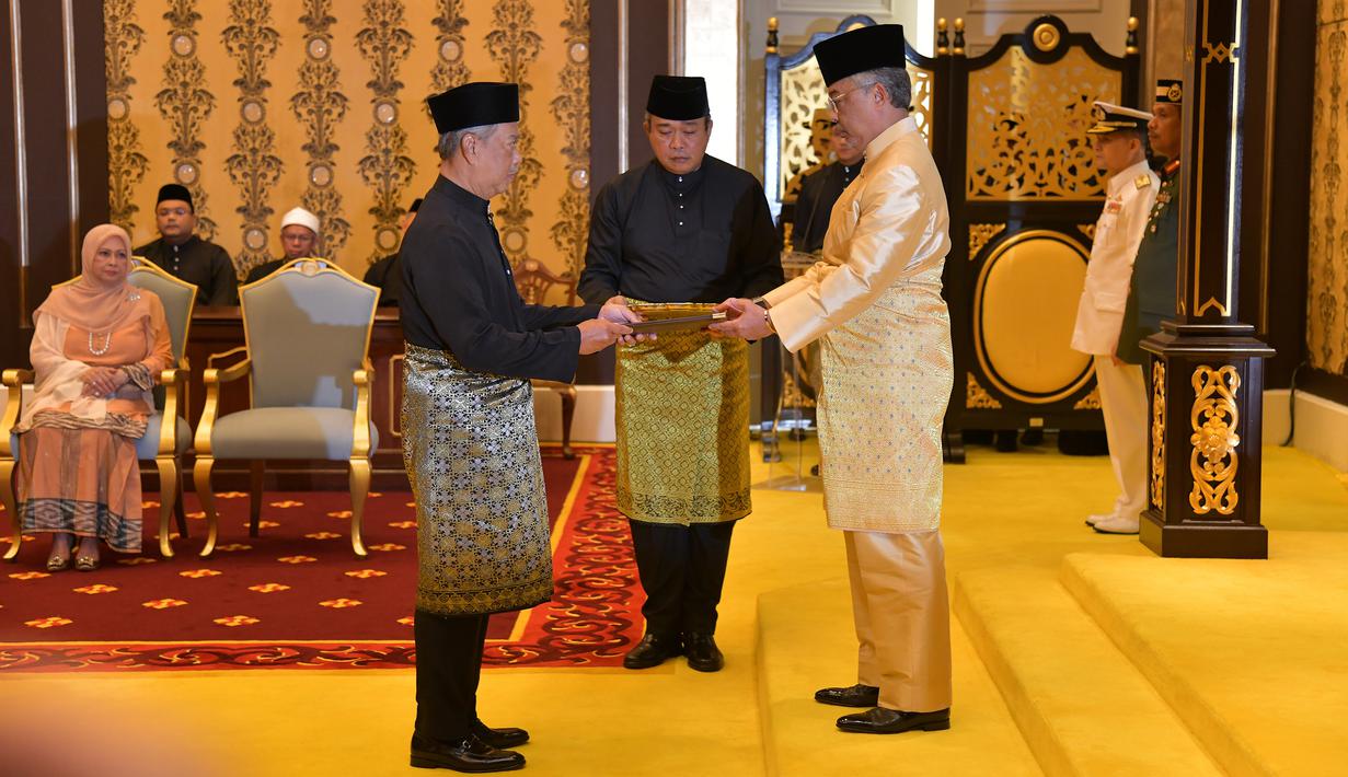 Muhyiddin Yassin (kiri) menerima dokumen dari Raja Sultan Abdullah Sultan Ahmad Shah (kanan) sebelum disumpah sebagai Perdana Menteri Malaysia di Istana Negara, Kuala Lumpur, Minggu (1/3/2020). Muhyiddin Yassin menggantikan Mahathir Mohamad. (MASZUANDI ADNAN/MALAYSIA'S DEPARTMENT OF INFORMATION/AFP)