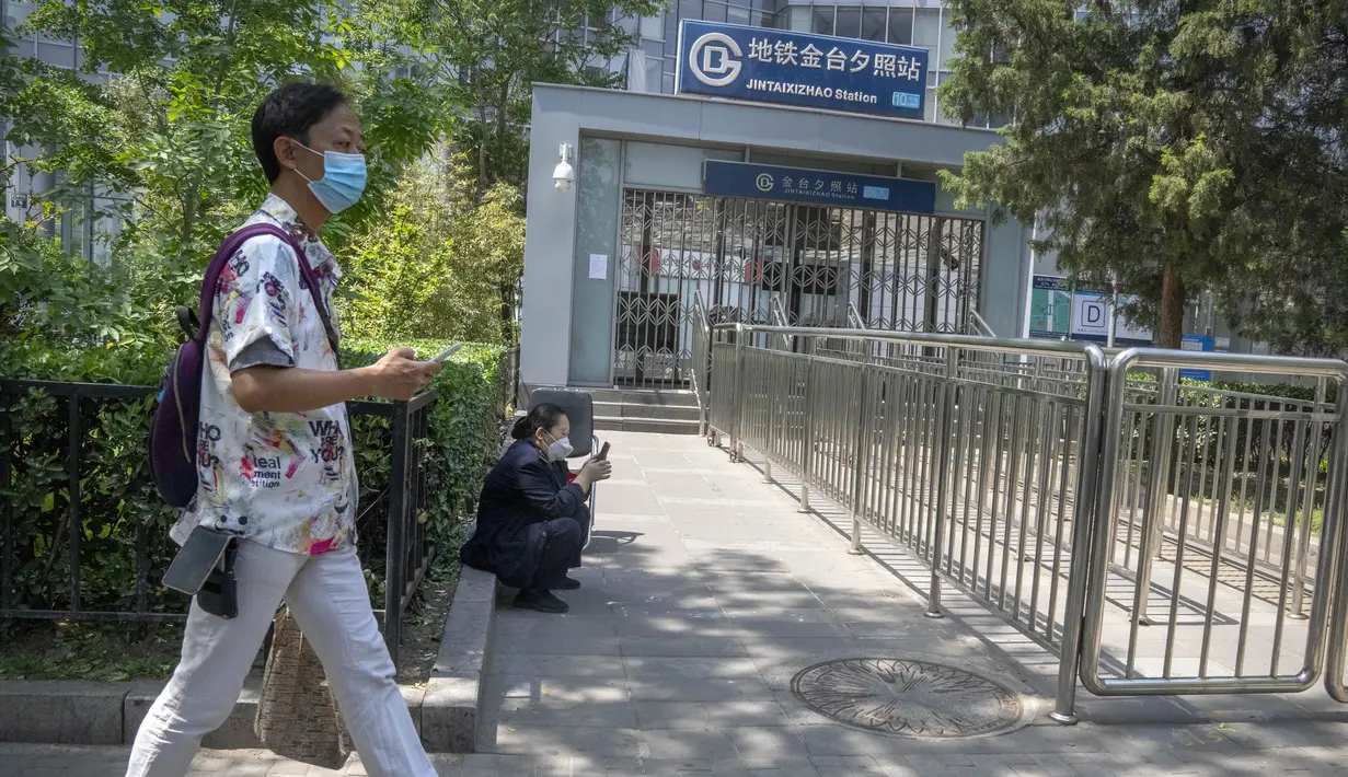 <p>Seorang pria yang mengenakan masker berjalan melewati pintu keluar stasiun kereta bawah tanah yang tertutup di Beijing, China Rabu (4/5/2022). Beijing pada hari Rabu ini menutup lebih dari 40 stasiun kereta bawah tanah, sekitar sepersepuluh dari jaringan kereta, sebagai bagian dari tindakan untuk menghentikan penyebaran Covid-19. (AP Photo/Mark Schiefelbein)</p>