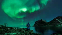 Seorang surfer membawa papannya melihat Cahaya Utara atau aurora borealis di Utakleiv, Norwegia utara (9/3). Biasanya aurora terjadi di daerah di sekitar kutub Utara dan kutub Selatan magnetiknya. (AFP/Olivier Morin)