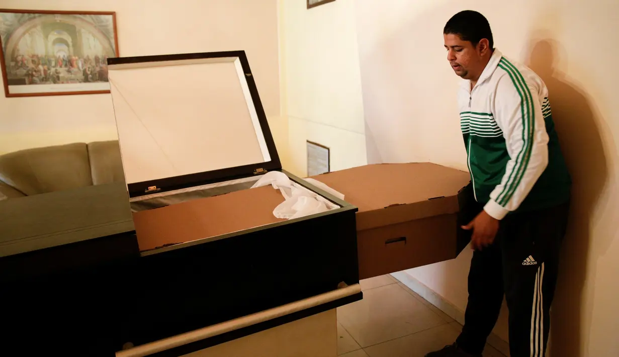 Seorang pria memasukkan peti mati karton ke dalam peti di kamar mayat di Valencia, negara bagian Carabobo, Venezuela, Kamis (25/08). Rakyat Venezuela kekurangan uang dan terpaksa mengubur mereka yang meninggal dalam kotak kardus. (REUTERS/Marco Bello).