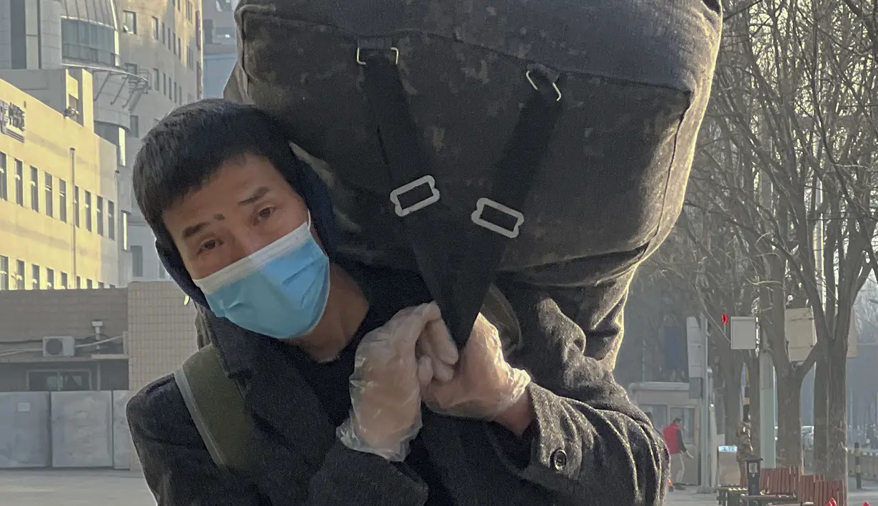 Seorang pekerja migran yang mengenakan masker dan sarung tangan membawa barang bawaannya saat tiba di Stasiun Kereta Api Barat di Beijing, Jumat (6/1/2023). China berupaya meminimalkan kemungkinan wabah COVID-19 yang lebih besar selama kesibukan perjalanan Tahun Baru Imlek bulan ini menyusul berakhirnya sebagian besar langkah-langkah pencegahan pandemi. (AP Photo/Wayne Zhang)