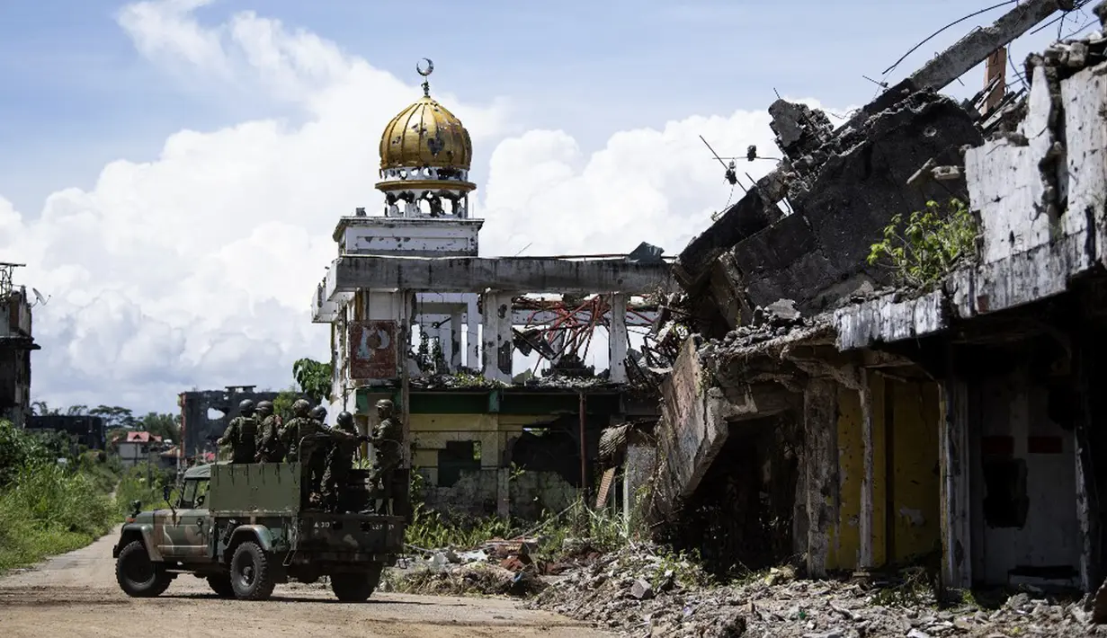 Tentara menaiki truk melewati bangunan yang hancur di Kota Marawi, Mindanao, Filipina, 23 Mei 2019. Kota yang sempat dikuasai ISIS tersebut tetap menjadi reruntuhan, para ahli pun memperingatkan bahwa upaya rekonstruksi yang macet memperkuat daya tarik kelompok ekstremis. (Noel CELIS/AFP)