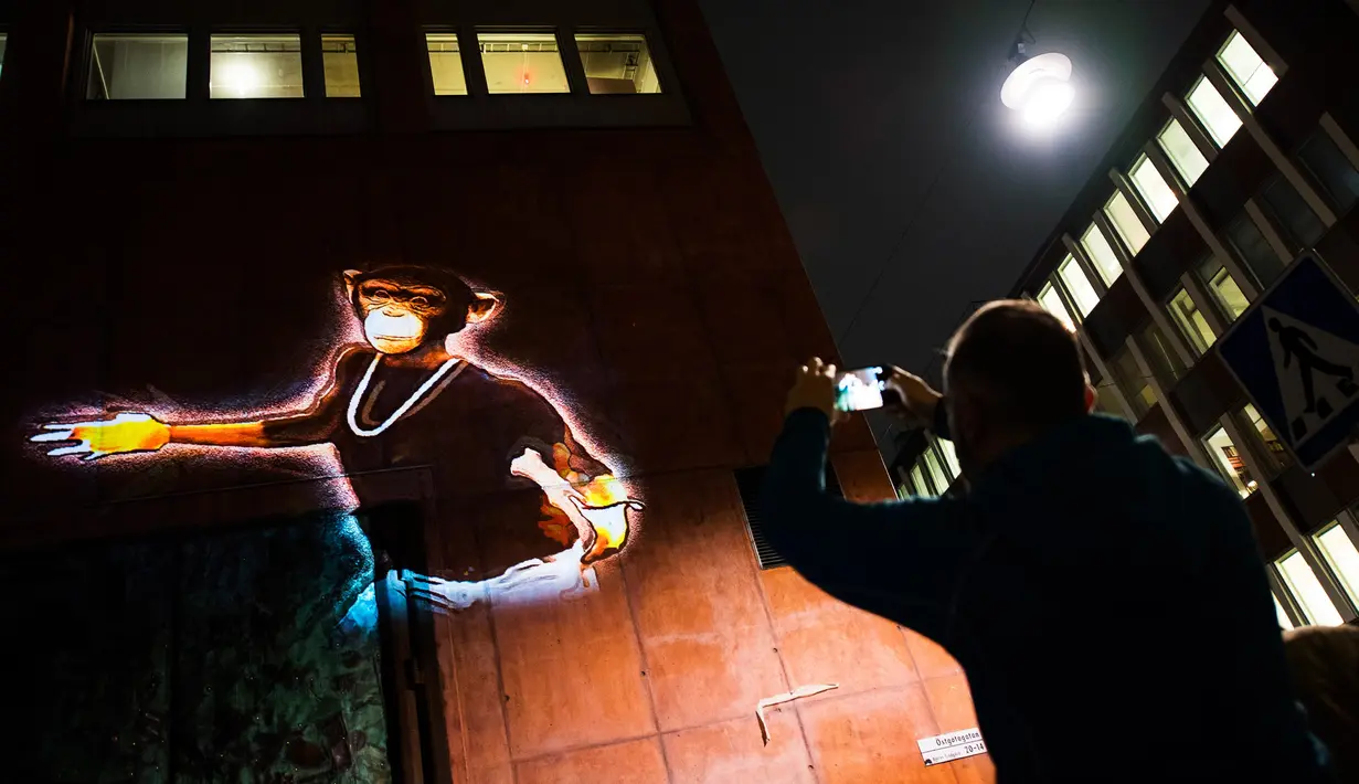 Seorang pria mengambil foto karya seniman Prancis, Julien Nonnon yang bergambar simpanse yang ditampilkan di tembok bangunan di Sodermalm, Stockholm, Swedia (25/11). (AFP/Jonathan Nackstrand)