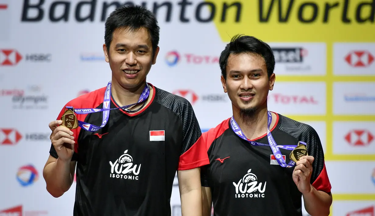 Ganda putra Indonesia Hendra Setiawan dan Mohammad Ahsan menunjukan medali emas usai babak final Kejuaraan Dunia Bulu Tangkis 2019 di St. Jakobshalle, Basel, Swiss, Minggu (25/8/2019). Ahsan/Hendra menjadi juara dunia ganda putra usai menang dengan skor 25-23, 9-21, 21-15. (FABRICE COFFRINI/AFP)