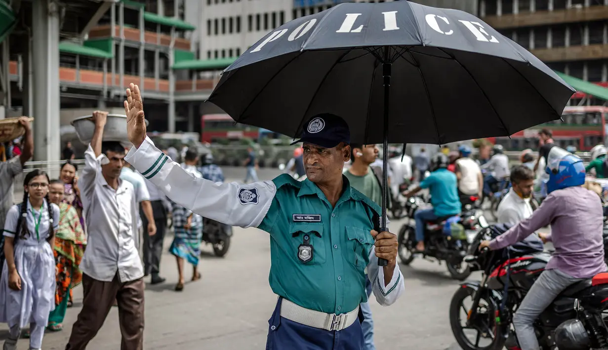 Seorang petugas polisi Bangladesh memegang payung untuk melindungi dirinya dari sengatan matahari saat mengatur lalu lintas di persimpangan jalan di Dhaka pada tanggal 12 Agustus 2024. (LUIS TATO/AFP)