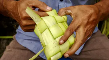 Seorang penjual menganyam daun kelapa atau kulit ketupat sambil menunggu pelanggan di sebuah pasar tradisional di Jakarta pada 2 April 2024. (BAY ISMOYO/AFP)