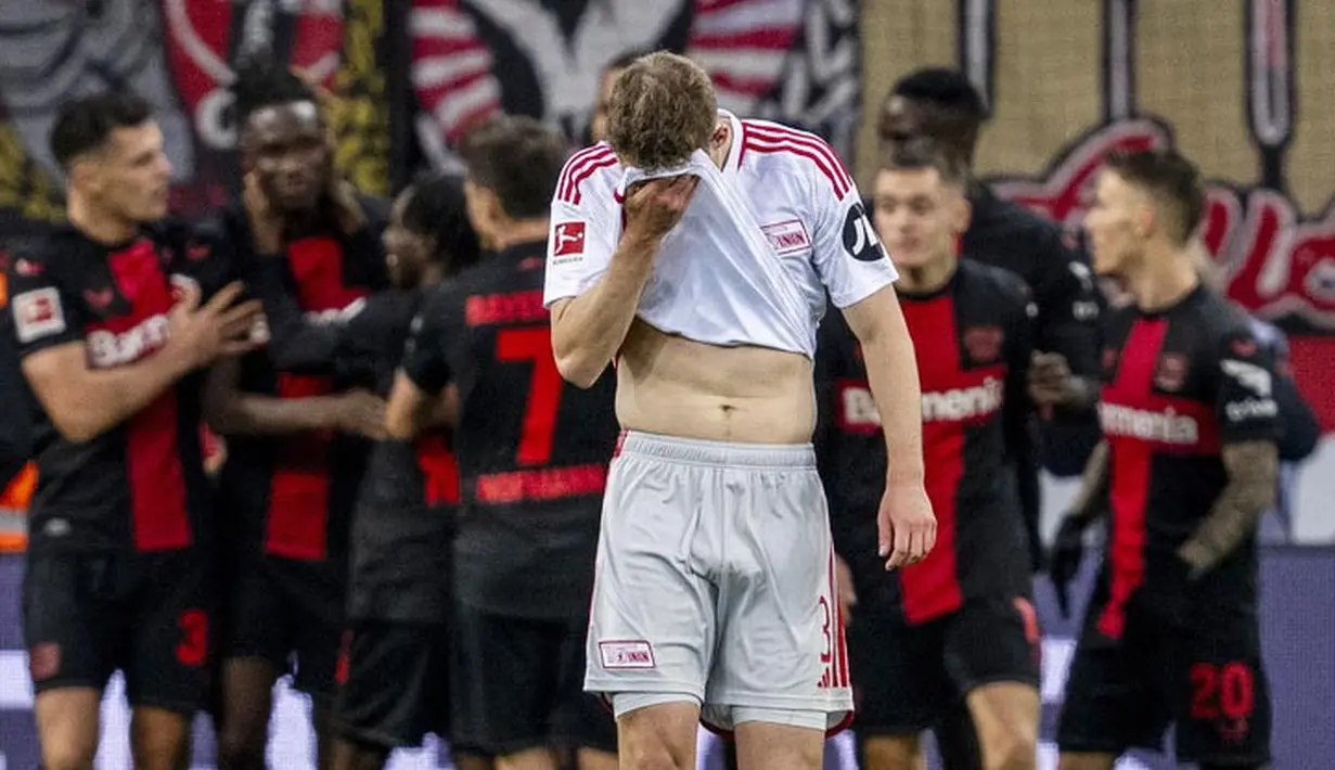 Pemain Union Berlin, Paul Jaeckel, menutup wajahnya saat pemain Bayer Leverkusen merayakan kemenangan pada laga Bundesliga di Bay Arena, Minggu (12/11/2023). (AFP/Ina Fassbender)