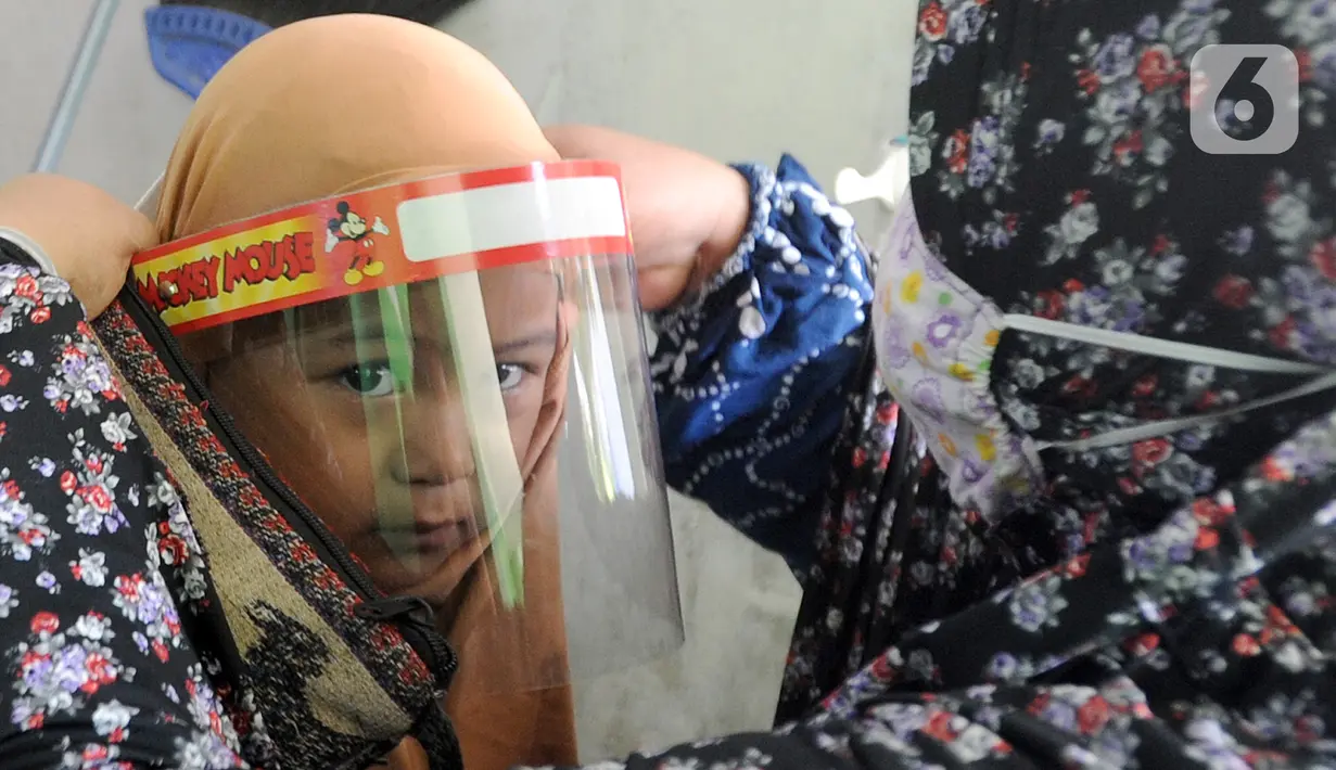 Seorang murid dipakaikan face shield sebelum belajar di Taman Pendidikan Al-Qur'an (TPA) Al-Muthmainnah Cinere, Depok, Rabu (1/7/2020). Proses belajar mengajar dilakukan dengan protokol kesehatan dimana murid diwajibkan menggunakan masker atau face shield. (merdeka.com/Arie Basuki)