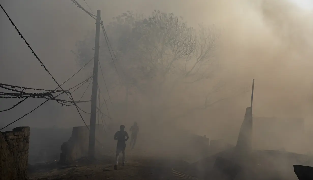 Orang-orang berlarian di tengah asap tebal selama kebakaran di daerah kumuh di Noida, pinggiran New Delhi, India, Minggu (11/4/2021). Dua anak tewas dan lebih dari 150 gubuk kumuh yang sebagian besar dihuni oleh para pemulung dalam kebakaran pada Minggu sore. (AP Photo/Altaf Qadri)