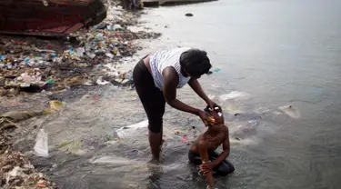 Seorang wanita memandikan putrinya di pantai saat mereka bersiap-siap untuk pergi ke gereja, di Warf of Port Cite Soleil di Port-au-Prince, Haiti (17/3). Cité Soleil merupakan lingkungan yang sangat miskin dan padat penduduk. (AP Photo/Dieu Nalio Chery)