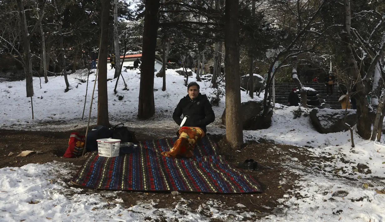 Seorang pria sedang piknik saat menghabiskan akhir pekannya di taman yang tertutup salju, di Teheran utara, Iran, Jumat (25/12/2020). Musim dingin di Iran biasanya dimulai dari bulan Desember hingga Februari.  (AP Photo/Vahid Salemi)