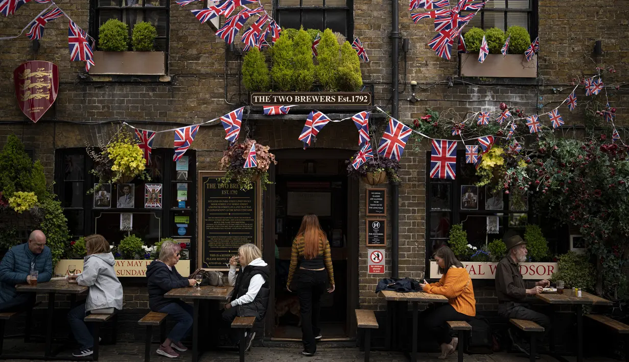 Pelanggan duduk di luar pub yang dihiasi bendera Union Jack dan gambar Raja Charles III, di Windsor, Inggris, Jumat, 5 Mei 2023. Penobatan Raja Charles III akan berlangsung di Westminster Abbey pada 6 Mei. (AP Photo/ Andreea Alexandru)
