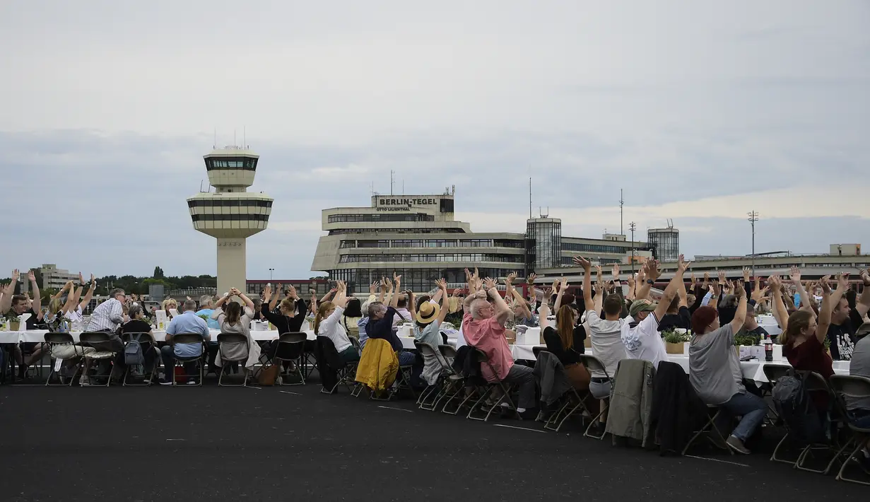Para tamu melambai ke arah helikopter yang terbang di atas meja mereka saat acara “Berlin Freedom Dinner” di landasan pacu bekas bandara Tegel, Berlin pada 7 Agustus 2021. Acara itu untuk mengirim sinyal 'Berlin kembali!' setelah berbulan-bulan menghadapi pandemi COVID-19. (Tobias SCHWARZ/AFP)