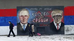 Sejumlah orang melintas di depan grafiti bergambar Donald Trump dan Vladimir Putin yang dirusak dengan cat di Belgrade, Serbia, Jumat (20/1). Diduga pelaku pengrusakan adalah mereka yang tak suka Trump menjadi Presiden AS. (AP Photo / Darko Vojinovic) 