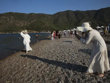 Seorang wanita mengambil foto saat orang-orang menikmati cuaca yang cerah, laut dan matahari, sehari sebelum jam malam hari Minggu di Adrasan, 100 kilometer barat Antalya, di Mediterania Turki, Sabtu (19/6/2021).  (AP Photo/Burhan Ozbilici)