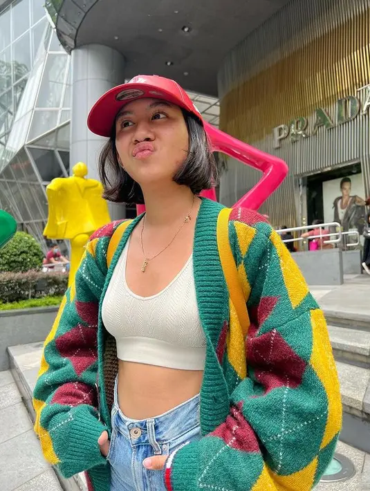 Di potret ini, Shenina tampil playful dengan mengenakan crop top putih yang dipadukan dengan jeans dan cardigan wool berwarna hijau bercorak kuning dan merah. (instagra/shenacinnamon)