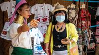 Perempuan Suku Kayan berbicara dengan turis yang mengenakan masker di sebuah toko suvenir di Taman Chang Siam, Pattaya, Thailand, Rabu (12/2/2020). Chang Siam Park adalah salah satu primadona bagi wisatawan China di Pattaya  yang kini berangsur sepi karena virus corona. (Mladen ANTONOV / AFP)