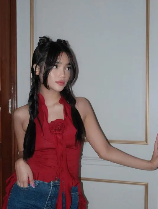 Ia tampil mengenakan asymmetric ruffle top warna merah merona dengan detail kerah halter neck dan aksen bunga di panel bagian depan. [@fuji_an].
