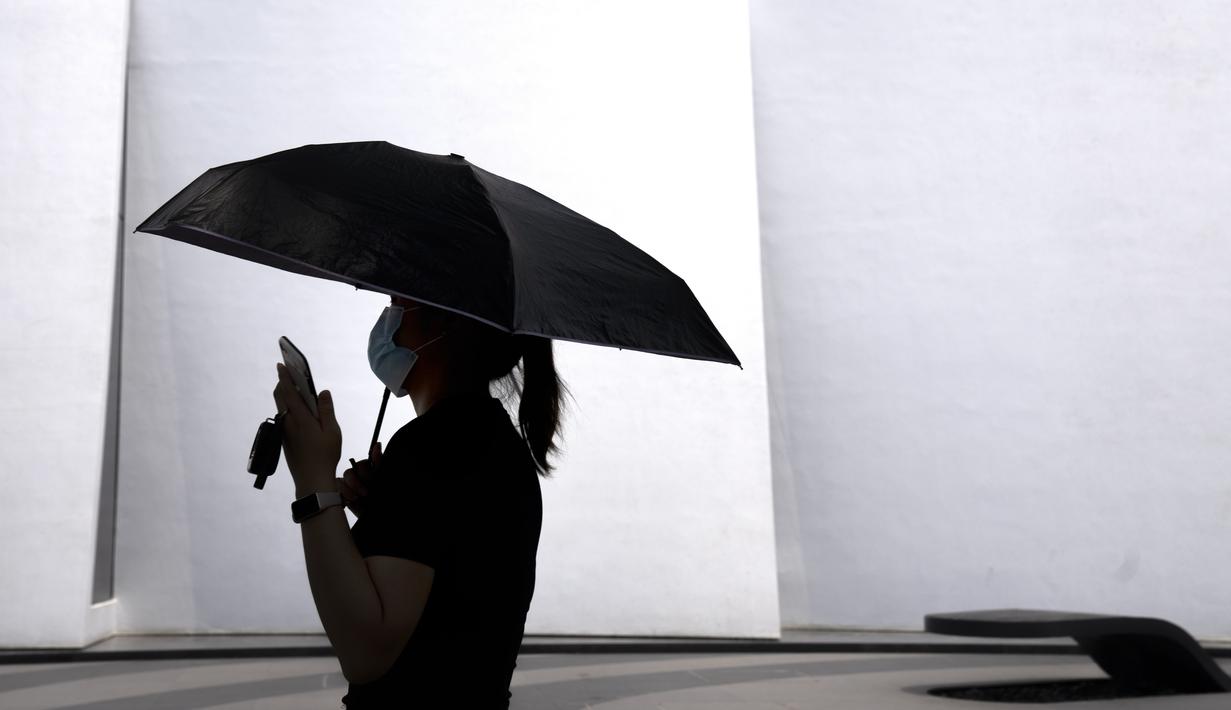 <p>Seorang perempuan membawa payung saat berjalan di sepanjang jalan di Beijing, Kamis (19/5/2022). Sebagian wilayah Beijing menghentikan pengujian massal harian yang telah dilakukan beberapa minggu terakhir, tetapi banyak tempat pengujian tetap sibuk karena syarat tes negatif COVID-19 dalam 48 jam terakhir untuk memasuki beberapa bangunan di ibu kota China. (AP Photo/Mark Schiefelbein)</p>