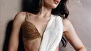 Detail busananya tampil lebih dekat di potret ini. Bra top bertabur kristal emas berpadu kain chiffon putih metalik yang berkilau lembut, lengkap dengan gelang cuff, cincin emas bertumpuk, dan lip gloss nude karamel. [@claurakiehl]
