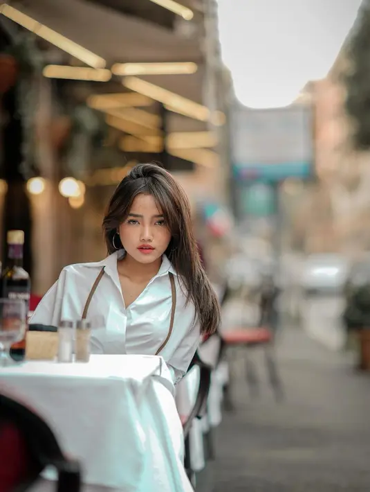 Ia tampil slay dengan busana netral bernuansa putih cokelat sambil ngopi di Italia [@fuji_an]