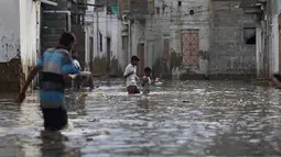 Warga melintasi jalan banjir setelah hujan deras di Karachi, Pakistan, Minggu, (26/7/2020). Sebagian warga memilih untuk bertahan meski rumah mereka terendam banjir. (AP Photo/Fareed Khan)