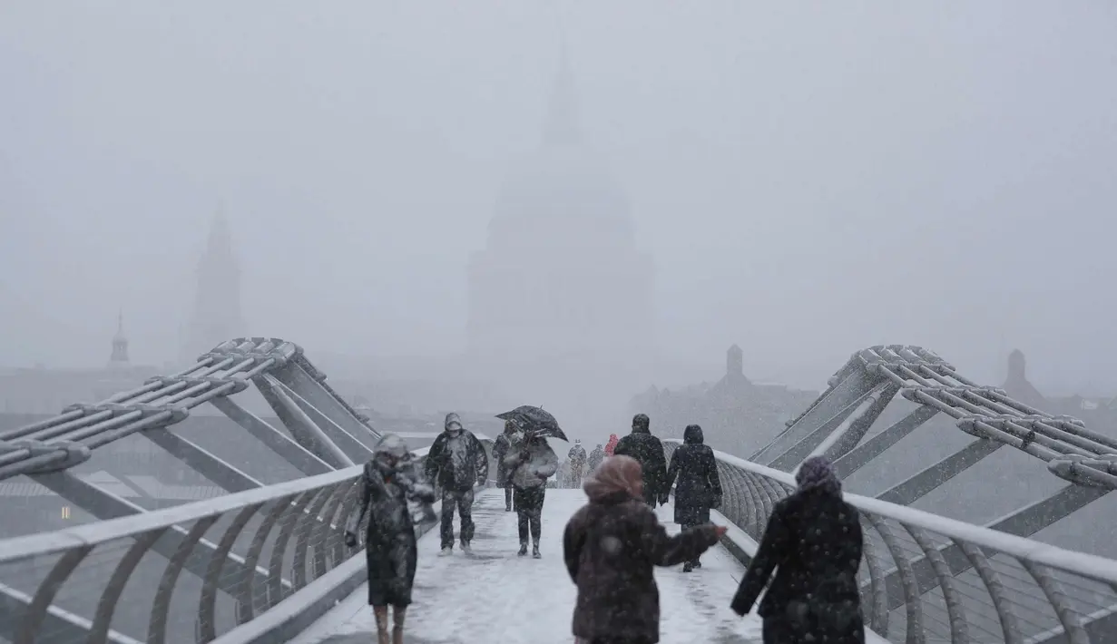 Pejalan kaki melintasi jembatan milenium dengan latar katedral St Paul saat hujan salju turun di London (27/2). (AFP Photo/Daniel Leal-Olivas)