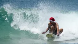 Seorang pria bertopi Santa memegang kamera aksi di giginya saat berselancar saat merayakan Natal di Pantai Bondi di Sydney, Sabtu (25/12/2021). (AP Photo/Rick Rycroft)