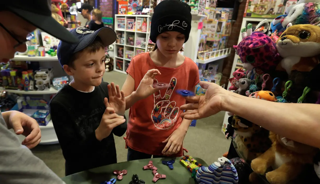 Dua orang anak memainkan fidget spinner di sebuah yang bernama toko Funky Monkey Toys di Oxford, Mich (11/5). Fidget spinner adalah sebuah mainan kecil yang bisa diputar dengan jari. (AP Photo / Carlos Osorio)