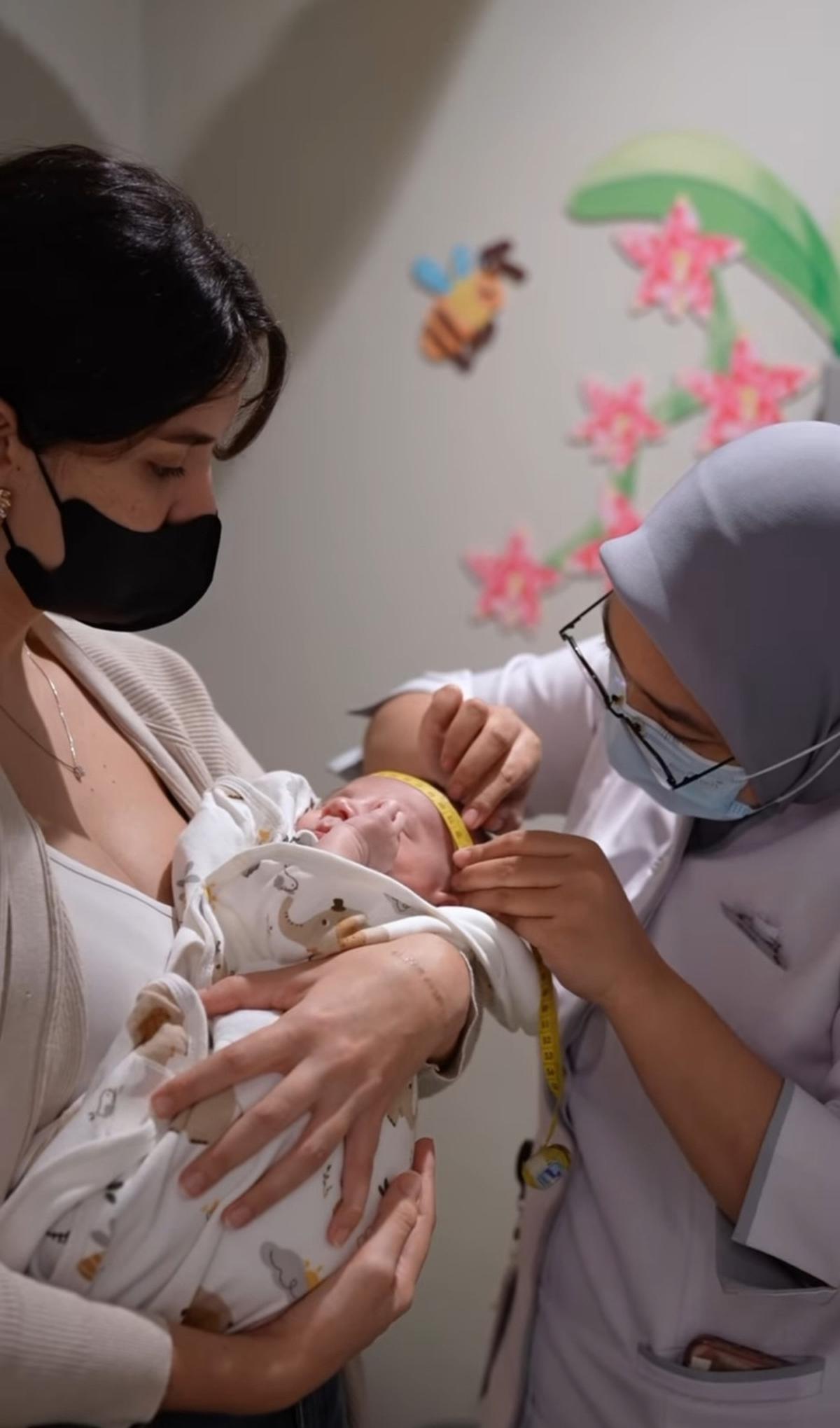 Sebagai ibu, Sarah benar-benar menggendong sang putra saat diperiksa oleh dokter. Ia bahkan memperhatikan tiap detail.