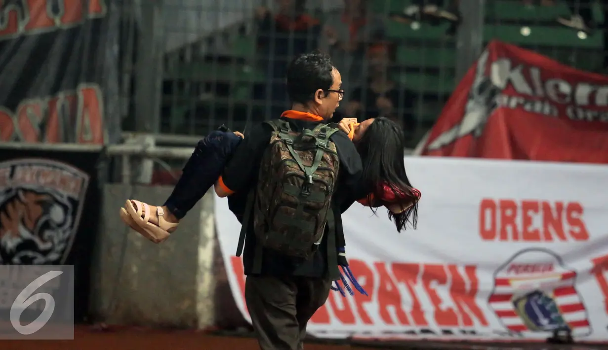 Suporter dievakuasi akibat asap tembakan gas air mata saat kericuhan dengan petugas kepolisian di laga Persija melawan Sriwijaya FC di Stadion GBK Jakarta, Jumat (24/6). Laga dihentikan di menit 81. (Liputan6.com/Helmi Fithriansyah)