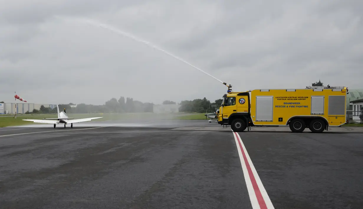 Sebuah truk pemadam kebakaran menyemprotkan pesawat Shark Ultralight milik Pilot Belgia-Inggris Zara Rutherford sebelum lepas landas di lapangan terbang Kortrijk-Wevelgem di Wevelgem, Belgia, Rabu (18/8/2021). (AP Photo/Virginia Mayo)