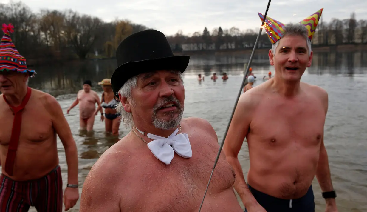 Anggota klub renang es "Berliner Seehunde" berenang menggunakan topi dan membawa kembang api di danau Orankesee, Berlin, Jerman (1/1). (REUTERS/Fabrizio Bensch)