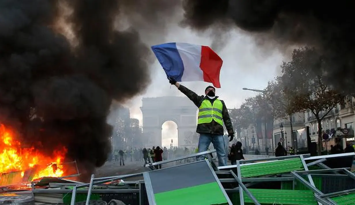 Demonstran mengibarkan bendera Prancis saat kerusuhan menentang kenaikan harga bahan bakar di Paris, Prancis, Sabtu (24/11). Demonstrasi terjadi oleh dorongan gerakan "rompi kuning". (AP Photo/Michel Euler)