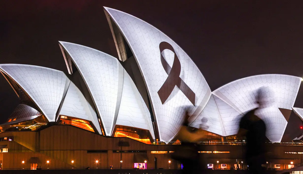 Orang-orang berjalan melewati pita hitam yang melambangkan kenangan dan duka cita diproyeksikan ke Sydney Opera House pada 9 Februari 2023 sebagai bentuk solidaritas terhadap Turki dan Suriah setelah gempa bumi dahsyat meluluhlantakkan kedua negara tersebut. (DAVID GRAY/AFP)