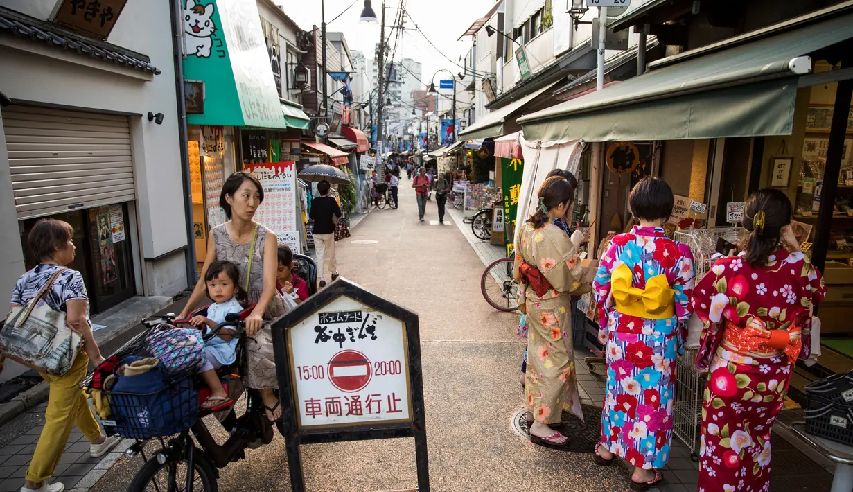 Seorang wanita mengendarai sepeda membawa anak-anaknya melihat ke arah sejumlah wanita yang mengenakan pakaian tradisional yang berbelanja di jalan Yanaka ginza di pusat Tokyo (30/9/2019). Wilayah Yanaka di ibukota Jepang dikenal sebagai salah satu yang paling kuno dan unik. (AFP Photo/Odd Andersen)