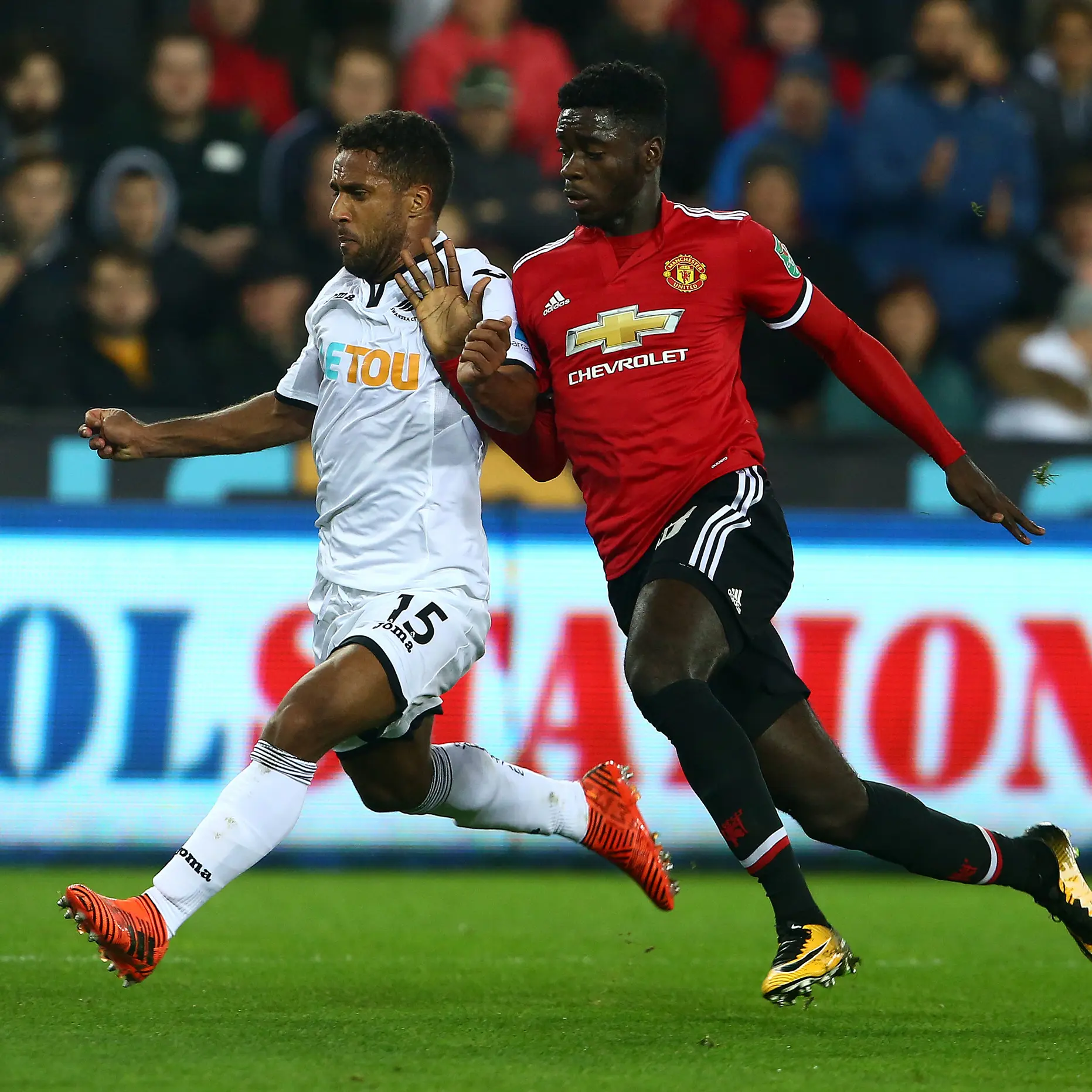 Pemain Manchester United, Axel Tuanzebe berebut bola dengan gelandang  Swansea City, Wayne Routledge pada pertandingan Piala Liga Inggris di Liberty Stadium, Rabu (25/10/2017). MU sukses menekuk Swansea City 2-0. (AFP/Geoff Caddick)