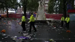 Petugas polisi berdiri di antara sampah yang ditinggalkan penggemar Skotlandia yang berpesta sebelum pertandingan grup D antara Inggris melawan Skotlandia di dekat patung William Shakespeare di Leicester Square di London, Jumat (18/6/2021). (AP Photo/Kirsty Wigglesworth)