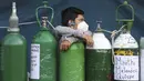 Seorang pemuda bersandar pada tabung oksigennya yang kosong saat menunggu toko isi ulang dibuka di lingkungan San Juan de Lurigancho di Lima, Peru, Senin (22/2/2021). Kekurangan oksigen medis untuk merawat pasien COVID-19 terus menjadi norma nasional. (AP Photo/Martin Mejia)