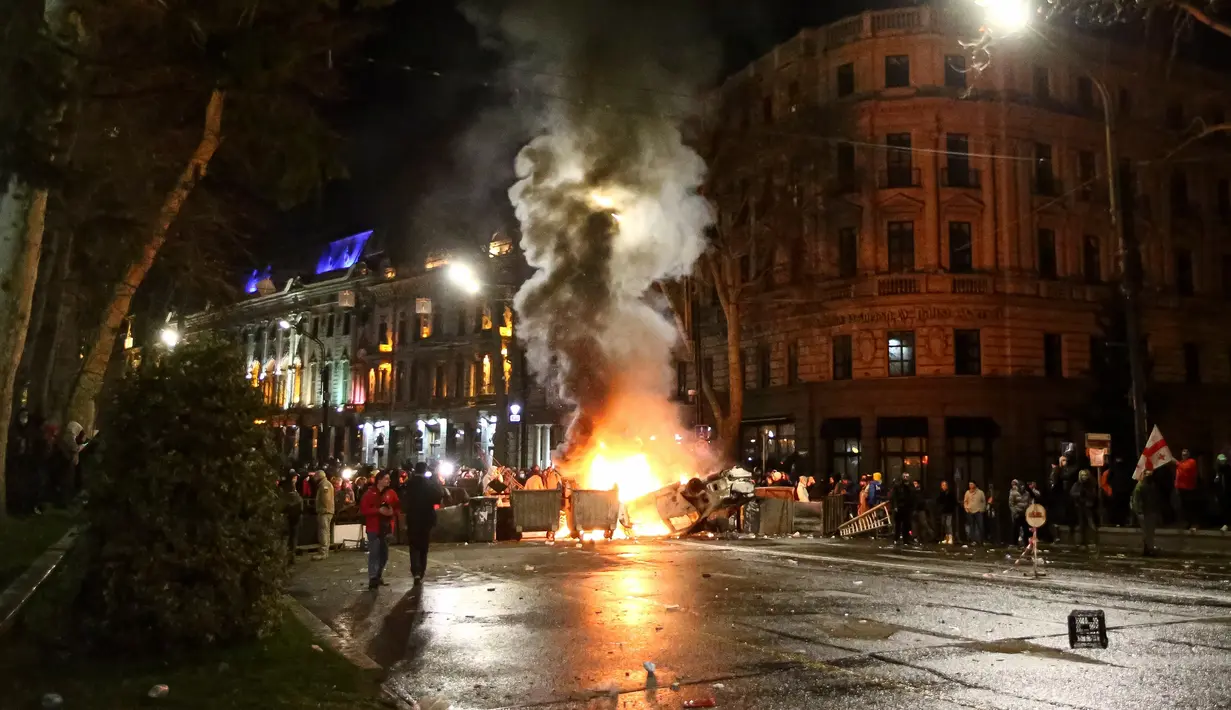 Para pengunjuk rasa berkumpul pada barikade dengan mobil polisi yang terbakar tidak jauh dari Gedung Parlemen Georgia di Tbilisi, Georgia, Kamis (9/3/2023). 
Para demonstran menganggap RUU "Agen Asing"  meniru undang-undang sejenis di Rusia yang bisa menghalangi Georgia bergabung dengan Uni Eropa, terutama setelah beberapa pejabat Uni Eropa mengkritik RUU itu. (AP Photo/Zurab Tsertsvadze)