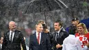 Presiden Rusia Vladimir Putin dilindungi oleh seorang pemandu yang memegang payung sementara para pejabat lainnya basah kuyup saat hujan turun selama penyerahan medali dan trofi Piala Dunia 2018 di Stadion Luzhniki, Minggu (15/7). (Kirill KUDRYAVTSEV/AFP)