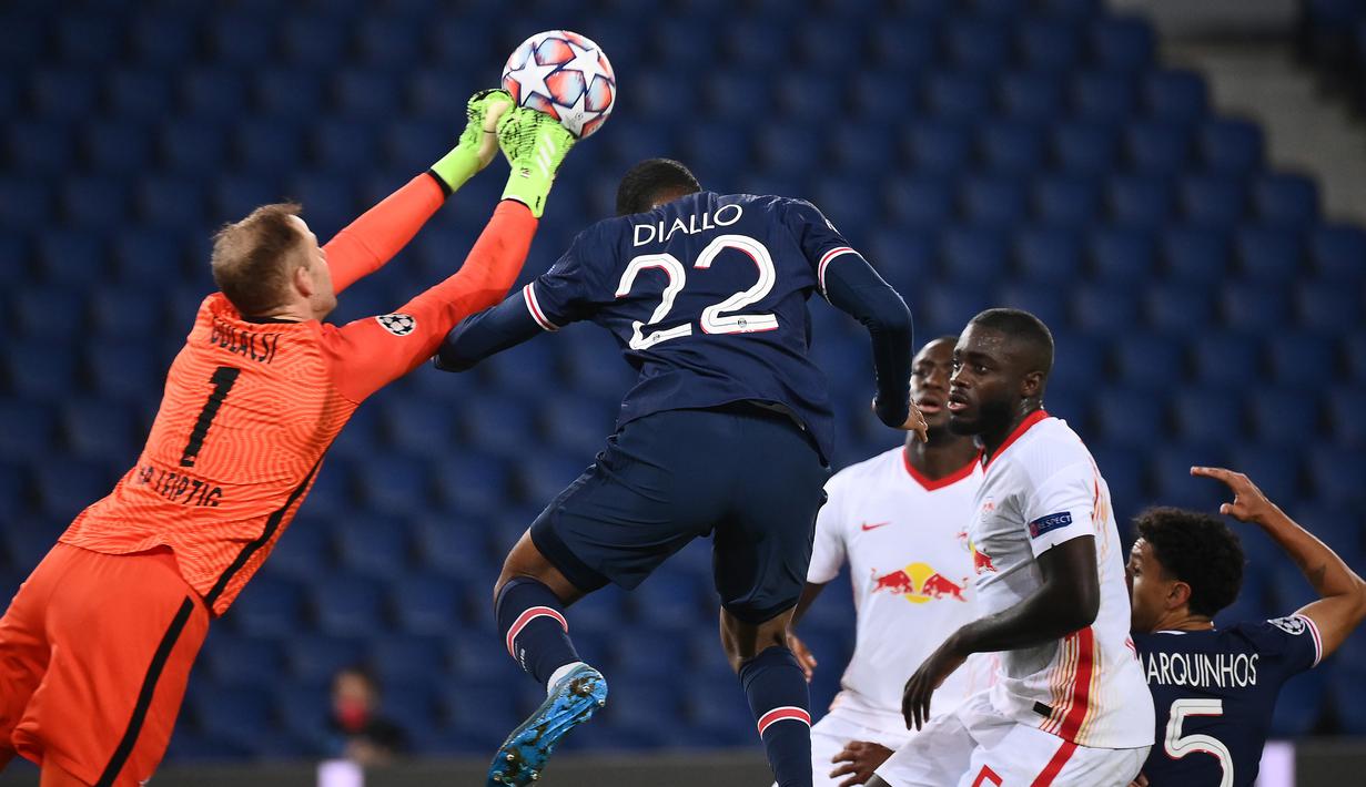Kiper RB Leipzig, Peter Gulacsi (kiri) meninju bola dari ancaman bek Paris Saint Germain, Abou Diallo, dalam laga lanjutan Liga Champions 2020/21 di Parc des Princes Stadium, Paris, Rabu (25/11/2020). Leipzig kalah 0-1 dari PSG. (AFP/Franck Fife)