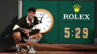 Carlos Alcaraz dari Spanyol berpose dengan trofi di samping jam yang menunjukkan durasi pertandingan, yang merupakan pertandingan final terlama di Roland-Garros, setelah menang melawan Jannik Sinner dari Italia di akhir pertandingan final tunggal putra mereka pada hari ke-15 turnamen tenis Prancis Terbuka di Lapangan Philippe-Chatrier di Kompleks Roland-Garros di Paris pada 8 Juni 2025. (Thibaud MORITZ/AFP)