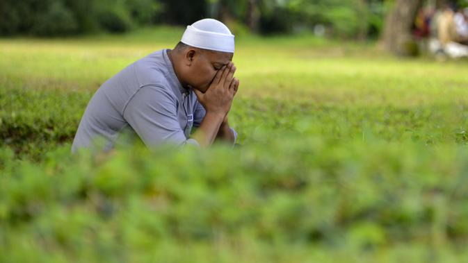 Seorang pria berdoa saat melakukan ziarah pada peringatan 16 tahun gempa bumi dan tsunami Aceh di sebuah kuburan massal di Siron, Sabtu (26/12/2020).  Peringatan di tengah pandemi COVID-19 itu tetap berlangsung secara sederhana melalui kegiatan ziarah kubur. (CHAIDEER MAHYUDDIN/AFP)