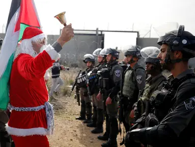 Seorang pengunjuk rasa berkostum Santa Claus menggelar aksi di desa Tepi Barat Bilin dekat Ramallah, Jumat (23/12). Mereka menentang pembangunan tembok pembatas di Israel. (REUTERS/Mohamad Torokman)