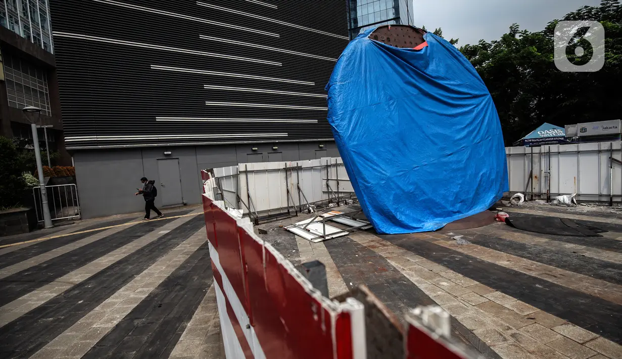 Warga melintas di dekat proyek Pembangunan tugu sepeda di Jalan Jenderal Sudirman, Jakarta, Rabu (30/3/2022). Tugu yang dulu sempat boming dan digembar-gemborkan kini terlihat terhenti pengerjaannya dan hanya ditutup terpal. (Liputa6.com/Johan Tallo)