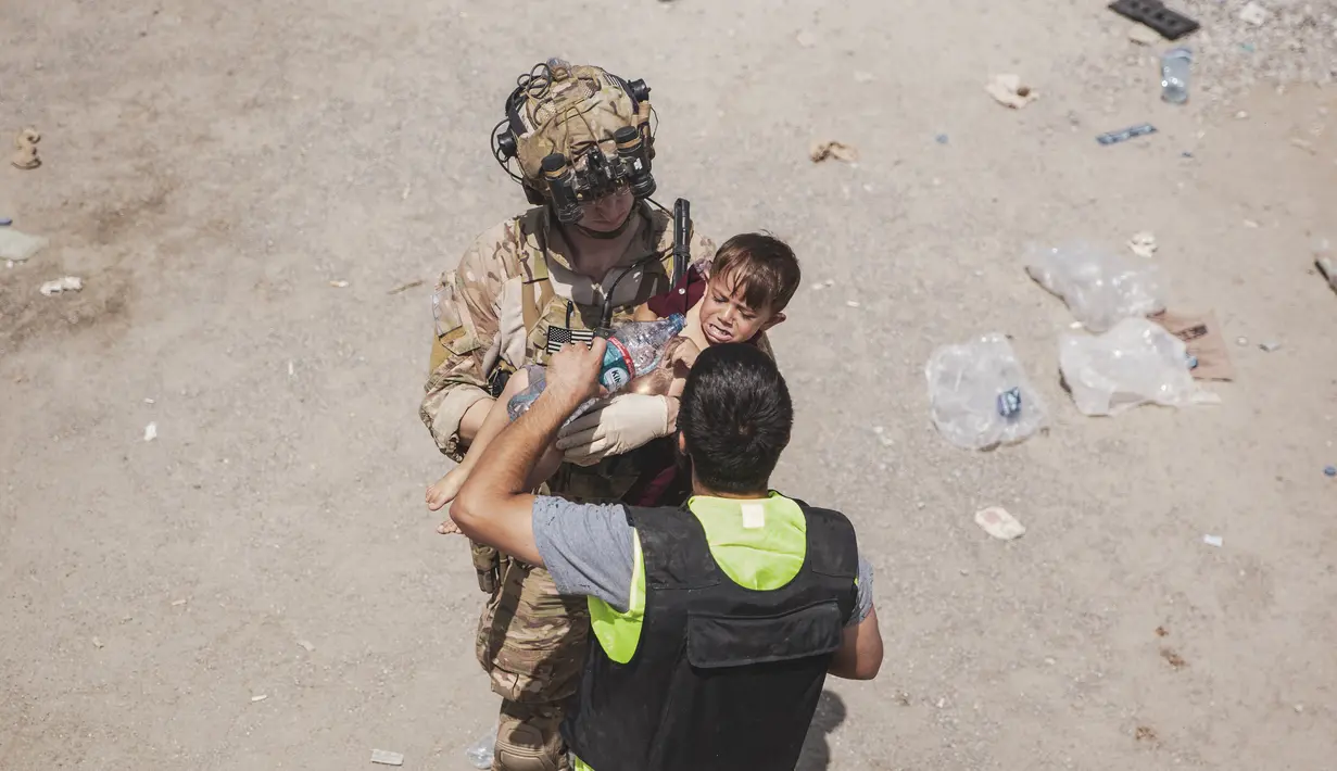 Tentara AS membawa seorang anak di pos pemeriksaan selama evakuasi di Bandara Internasional Hamid Karzai di Kabul, Jumat (20/8/2021). Sejumlah ibu Afghanistan berupaya menyerahkan bayi-bayi mereka pada tentara asing yang berjaga di bandara. (Staff Sgt. Victor Mancilla/U.S. Marine Corps via AP)