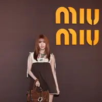 Momo TWICE tampil dengan gaya playful bernuansa vintage. Ia mengenakan mini dress cokelat bersiluet babydoll yang dipadukan dengan panel rajut krem pada bagian atas. Aksen scarf bermotif warna-warni di leher menambah sentuhan retro yang khas. [Dok/Miu Miu].