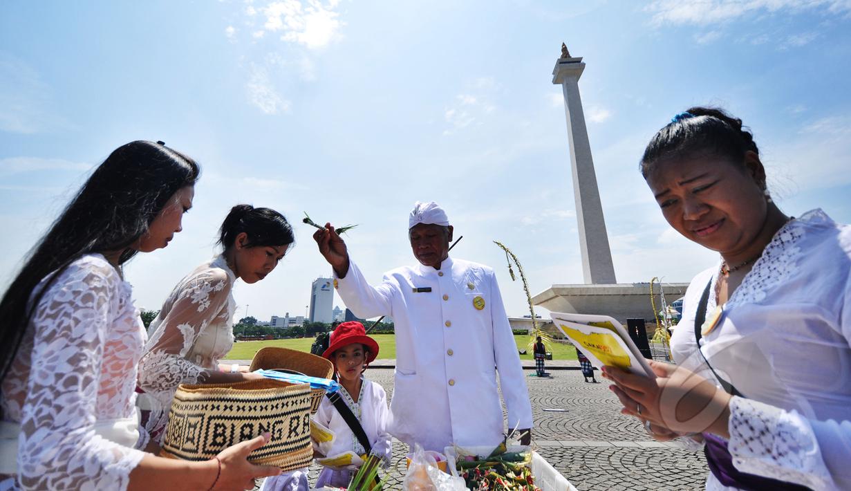 Pemuka agama mencipratkan air suci pada umat Hindu yang akan mengikuti upacara Tawur Agung Kesanga di Silang Monas, Jakarta, Jumat (20/3). Upacara tersebut untuk membersihkan jagat raya sebelum pelaksanaan Nyepi esok harinya.  (Liputan6.com/Faizal Fanani)