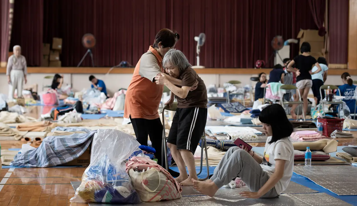 Pengungsi tua berusaha berdiri dari duduknya di lokasi pengungsian di Mabi, Prefektur Okayama, Jepang, Rabu (11/7). Pemerintah Jepang menyatakan banjir disertai tanah longsor telah menewaskan 179 orang. (Martin BUREAU/AFP)
